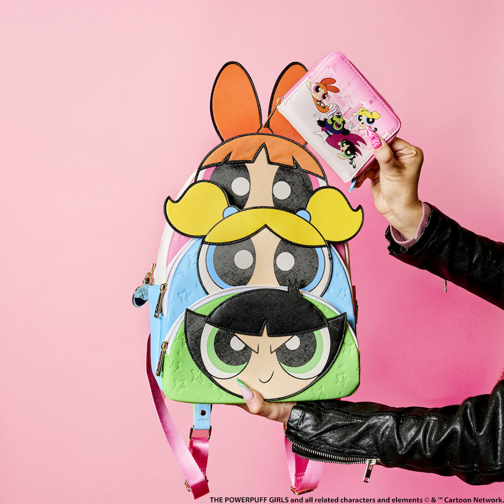 Two hands holding the Powerpuff Girls Triple Pocket Backpack and Powerpuff Girls vs. Mojo Jojo Zip Around Wallet against a pink background